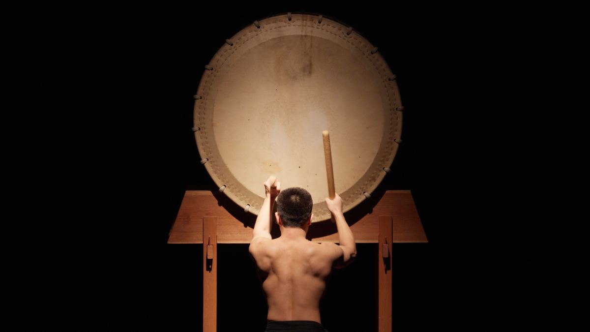 Percussionista de taikô diante de um grande tambor iluminado